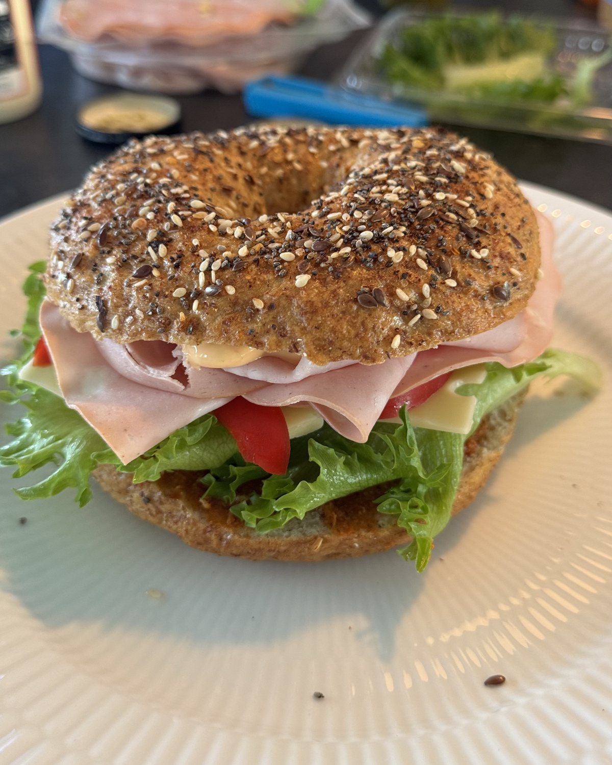 Hjemmebagt bagel med frø, fyldt med skinke, ost, salat og tomat