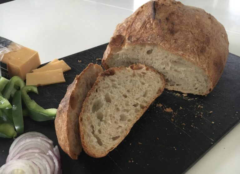 Jespers spanske bondebrød skåret i skiver på et sort skærebræt med ost, peberfrugt og rødløg